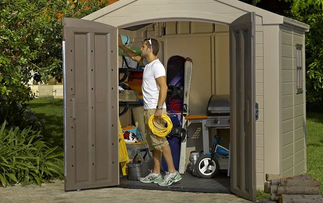 Man organizing items inside a storage shed with tools and furniture.