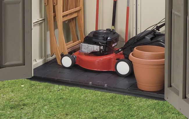 Red lawn mower inside a storage shed with gardening tools and a pot.