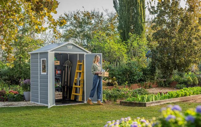 Woman opening a garden shed door in a garden setting with trees and plants.