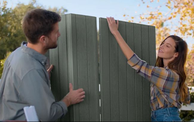 Two people interacting with a green metal fence panel outdoors.