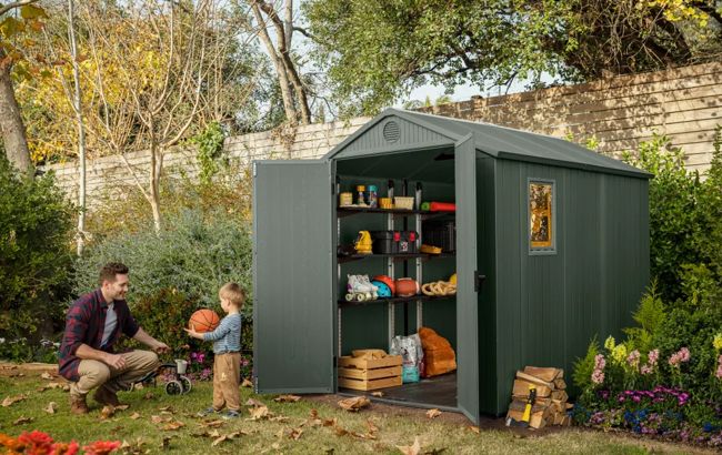 Green storage shed in a garden with a man and child playing outside