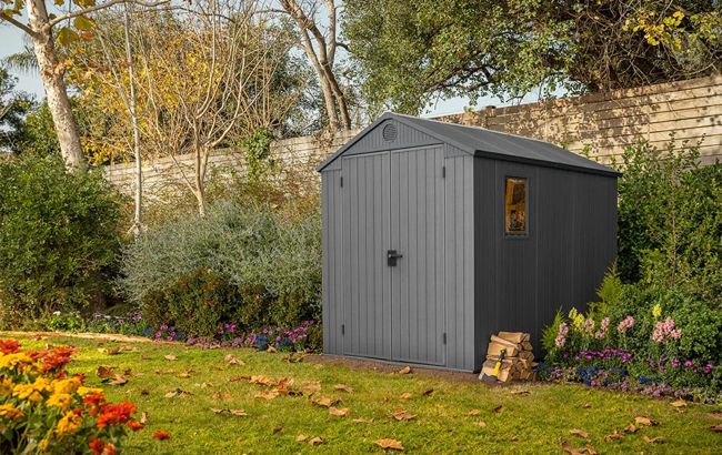 Gray storage shed in a garden with flowers and trees
